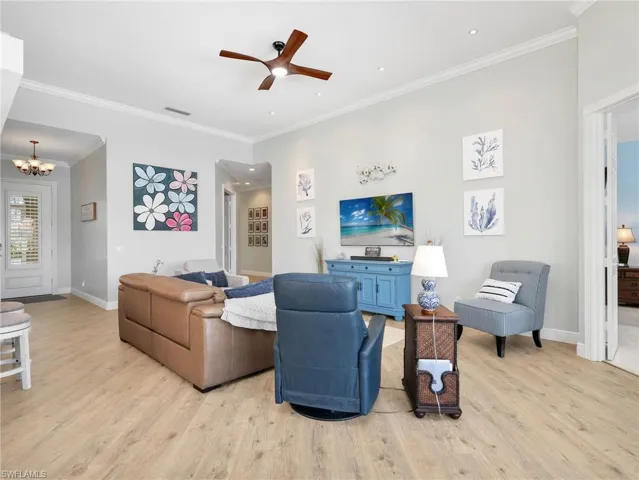 Living room featuring ornamental molding, a ceiling fan, light wood-style flooring, and suspended lighting