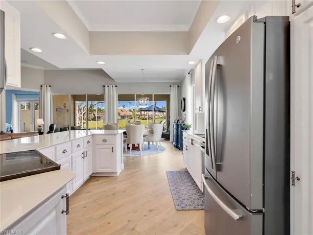 Kitchen with freestanding refrigerator, white cabinetry, crown molding, light stone counters, and light wood-style flooring