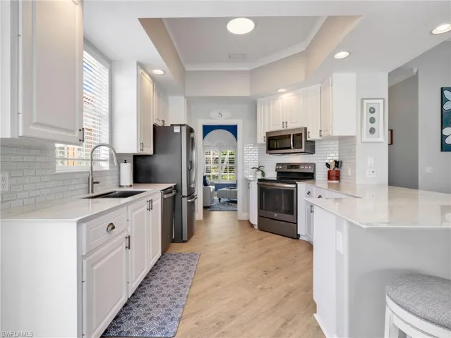 Kitchen with a peninsula, white cabinets, stainless steel appliances, light stone countertops, and crown molding