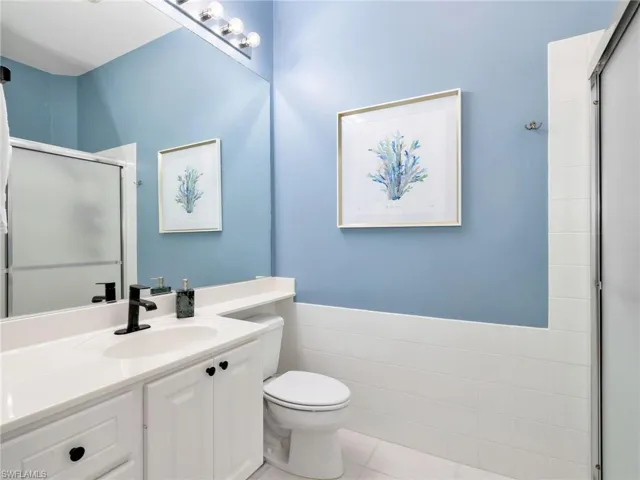 Bathroom featuring a shower stall, vanity, tile walls, light tile patterned floors, and a wainscoted wall