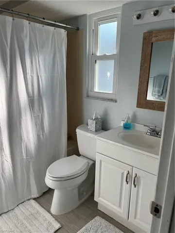Full bathroom with a textured ceiling, toilet, vanity, and shower / bathtub combination with curtain