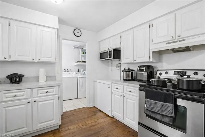Kitchen with stainless steel appliances, white cabinetry, light countertops, and independent washer and dryer