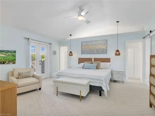 Bedroom with a barn door, access to outside, light colored carpet, a ceiling fan, and vaulted ceiling