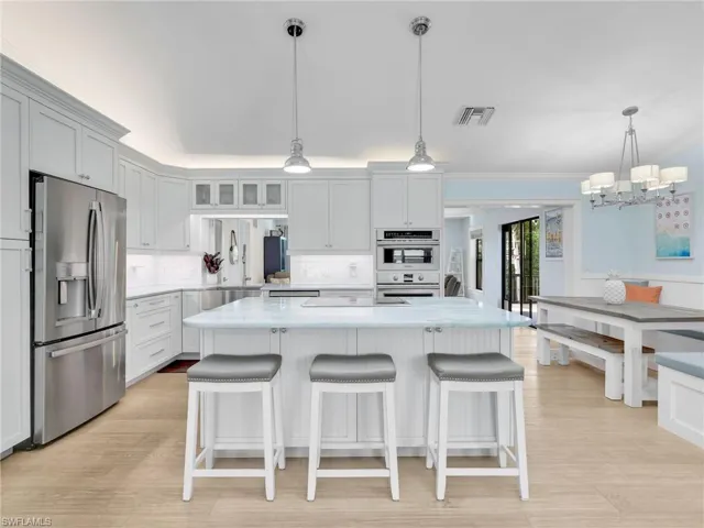 Kitchen with appliances with stainless steel finishes, glass insert cabinets, decorative light fixtures, a breakfast bar area, and white cabinets