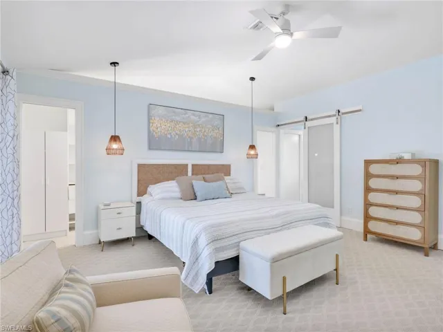 Carpeted bedroom featuring ensuite bathroom, a barn door, ceiling fan, and crown molding
