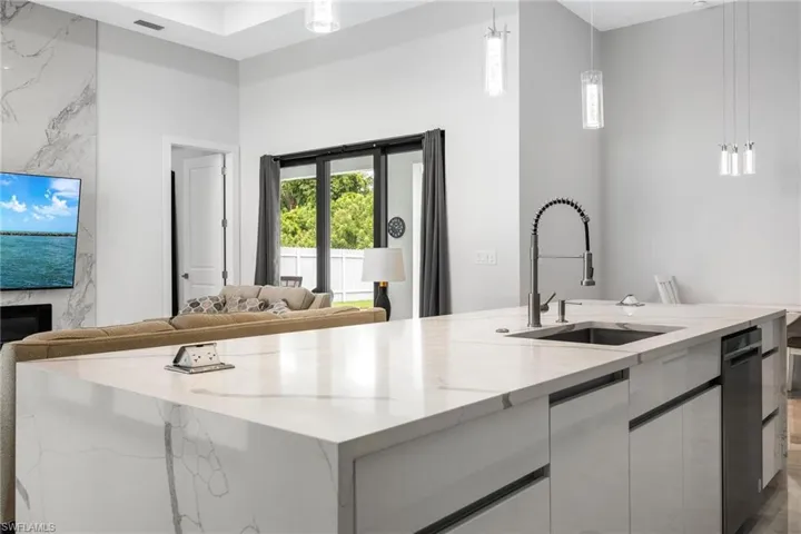Kitchen with hanging light fixtures, open floor plan, light stone counters, white cabinetry, and a kitchen island with sink