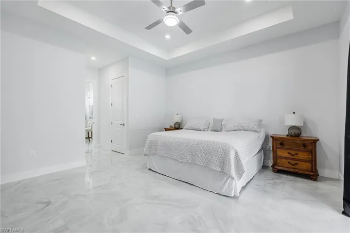 Bedroom with a tray ceiling, ceiling fan, marble finish flooring, and recessed lighting