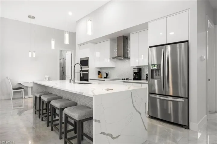 Kitchen featuring stainless steel appliances, decorative light fixtures, white cabinets, tasteful backsplash, and wall chimney exhaust hood