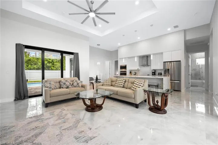 Living room with a towering ceiling, a tray ceiling, light marble finish floors, a ceiling fan, and recessed lighting