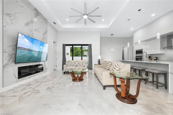 Living room with a tray ceiling, ceiling fan, recessed lighting, and light marble finish floors