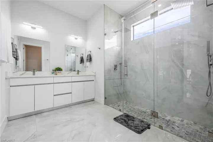 Bathroom featuring a marble finish shower, double vanity, and light marble finish floors