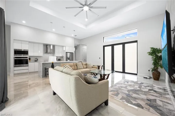 Living area with a raised ceiling, a towering ceiling, ceiling fan, recessed lighting, and light marble finish floors