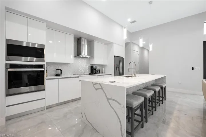 Kitchen with decorative backsplash, white cabinetry, appliances with stainless steel finishes, modern cabinets, and a towering ceiling