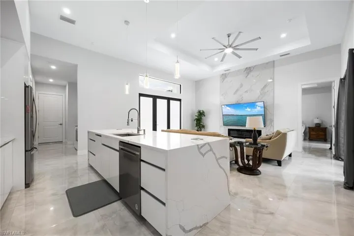 Kitchen featuring modern cabinets, white cabinets, light stone countertops, hanging light fixtures, and recessed lighting