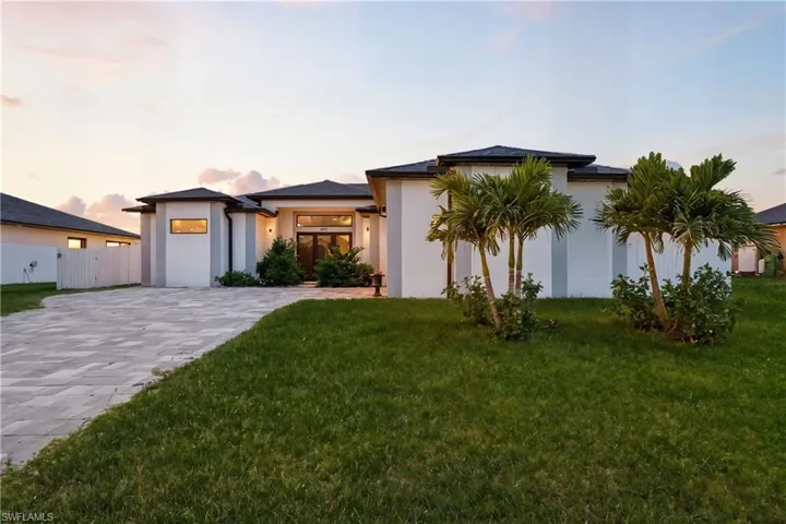 View of front facade featuring stucco siding, a yard, and decorative driveway