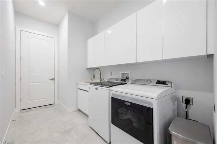 Laundry room featuring light marble finish flooring, washing machine and clothes dryer, and cabinet space