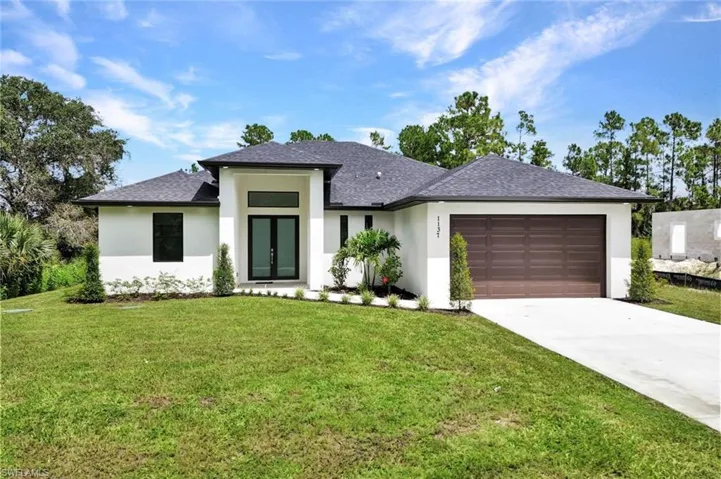 Prairie-style home with a front lawn, stucco siding, a shingled roof, and driveway