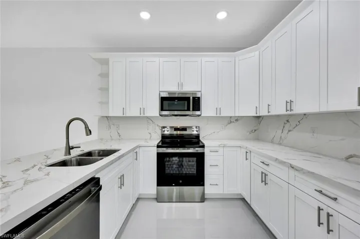Kitchen with stainless steel appliances, open shelves, light stone counters, white cabinetry, and backsplash