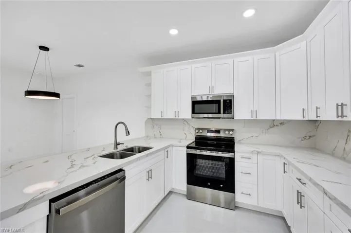 Kitchen featuring stainless steel appliances, light stone counters, white cabinetry, pendant lighting, and tasteful backsplash