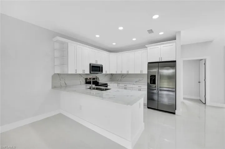 Kitchen with open shelves, stainless steel appliances, white cabinetry, light stone countertops, and tasteful backsplash