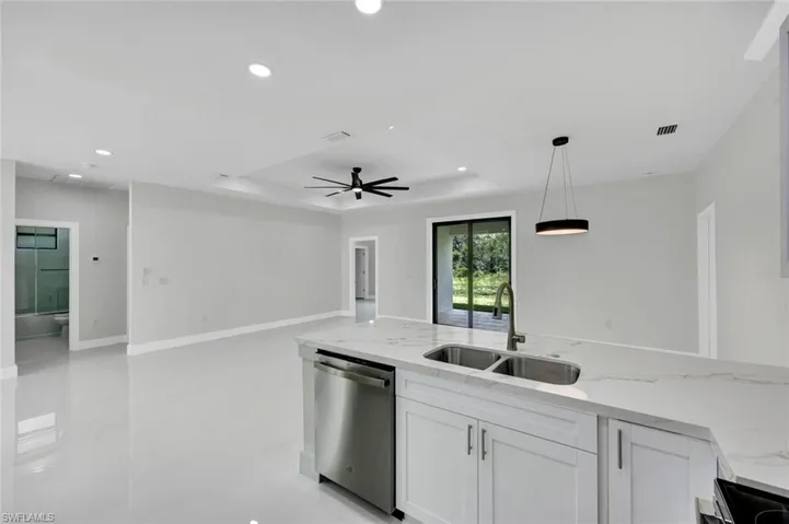 Kitchen featuring light stone counters, dishwasher, open floor plan, pendant lighting, and white cabinetry
