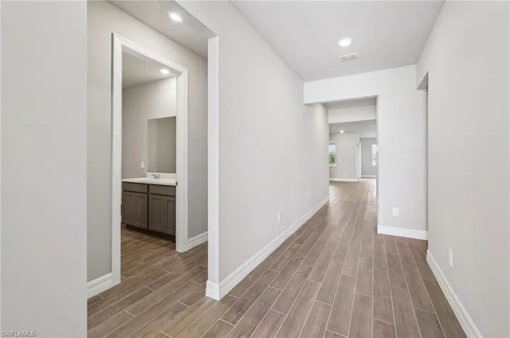 Hall featuring wood finished floors, baseboards, recessed lighting, and a sink