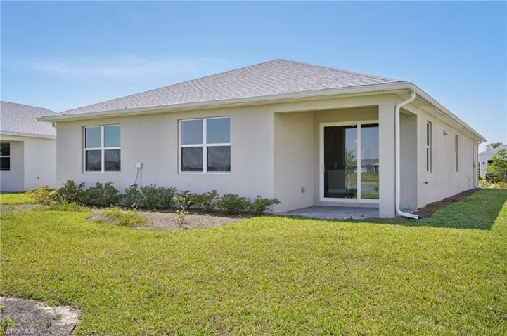 Rear view of house featuring stucco siding, a lawn, and roof with shingles