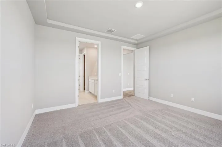 Unfurnished bedroom with light carpet, baseboards, ensuite bath, and recessed lighting