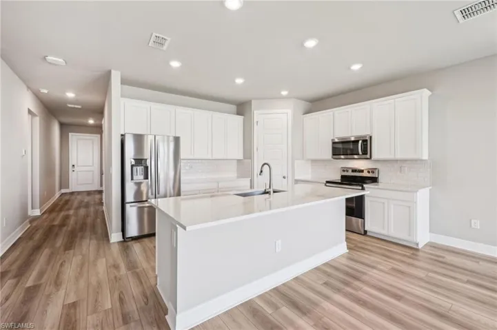 Kitchen with appliances with stainless steel finishes, a sink, decorative backsplash, light wood finished floors, and white cabinetry