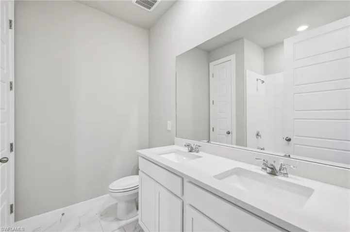 Bathroom with baseboards, toilet, a shower, marble look tiles, and double vanity