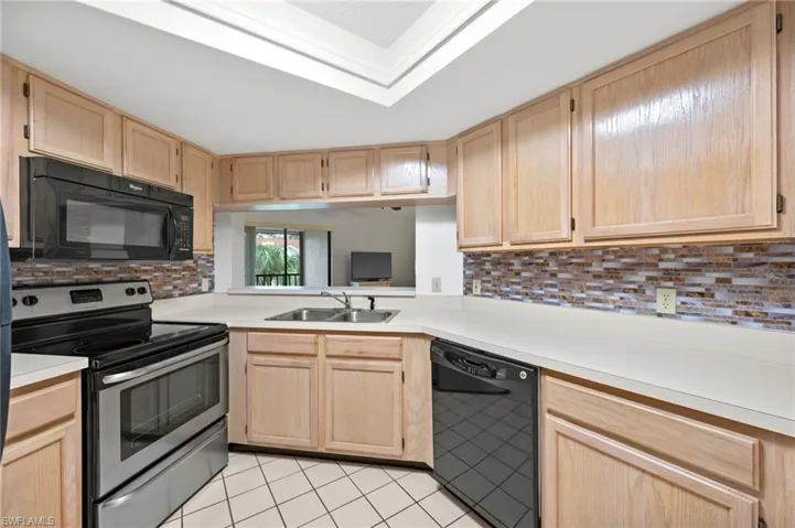 Kitchen featuring black appliances, light brown cabinetry, light countertops, backsplash, and light tile patterned floors