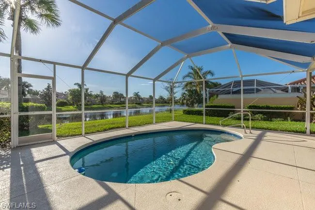 View of pool with glass enclosure, a water view, and a patio area