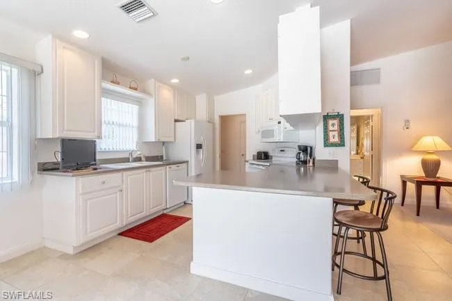 Kitchen featuring white cabinetry, kitchen peninsula, a kitchen breakfast bar, light tile patterned floors, and white appliances