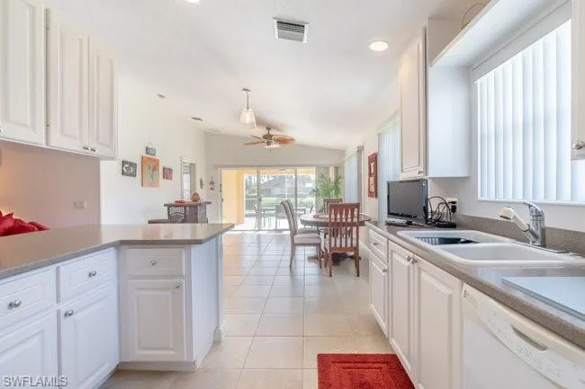 Kitchen with lofted ceiling, dishwasher, sink, light tile patterned floors, and white cabinetry