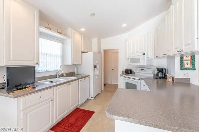 Kitchen featuring white cabinets, kitchen peninsula, light tile patterned floors, sink, and white appliances