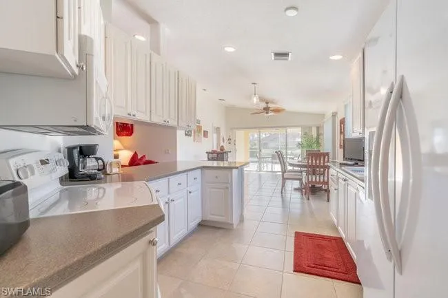 Kitchen featuring light tile patterned flooring, white cabinetry, kitchen peninsula, white appliances, and vaulted ceiling