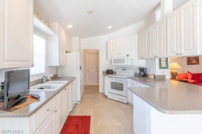 Kitchen with sink, kitchen peninsula, light tile patterned floors, white appliances, and white cabinets
