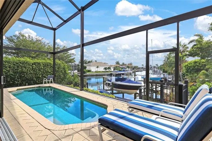View of swimming pool featuring a dock, glass enclosure, a water view, and a patio