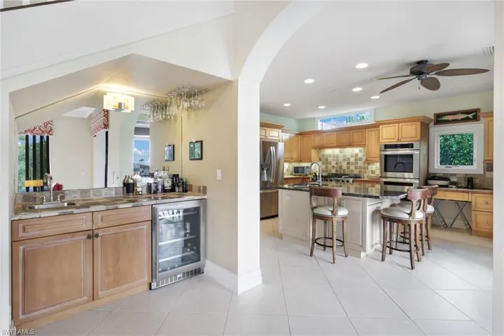 Kitchen featuring ceiling fan, a kitchen breakfast bar, an island with sink, stainless steel appliances, and beverage cooler