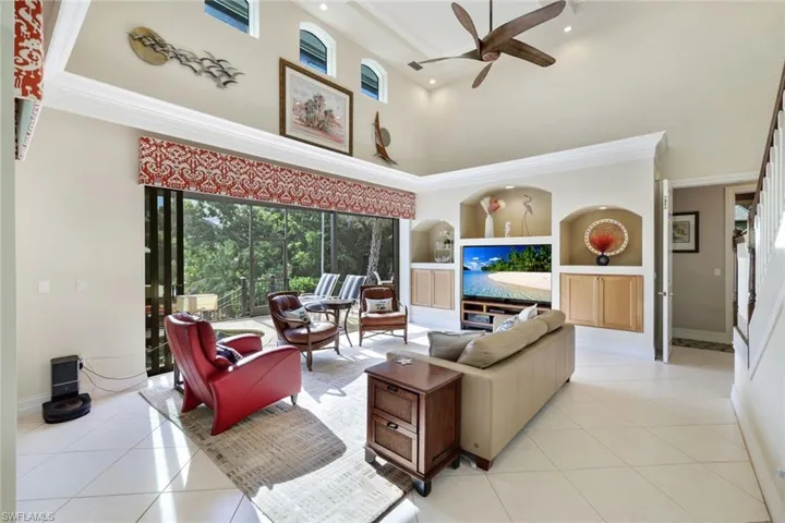 Living room featuring light tile patterned floors, ornamental molding, built in features, ceiling fan, and a towering ceiling