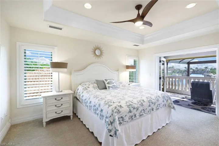 Carpeted bedroom featuring ceiling fan, access to outside, and a tray ceiling