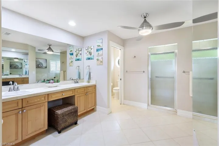 Bathroom with toilet, dual bowl vanity, ceiling fan, tile patterned floors, and walk in shower