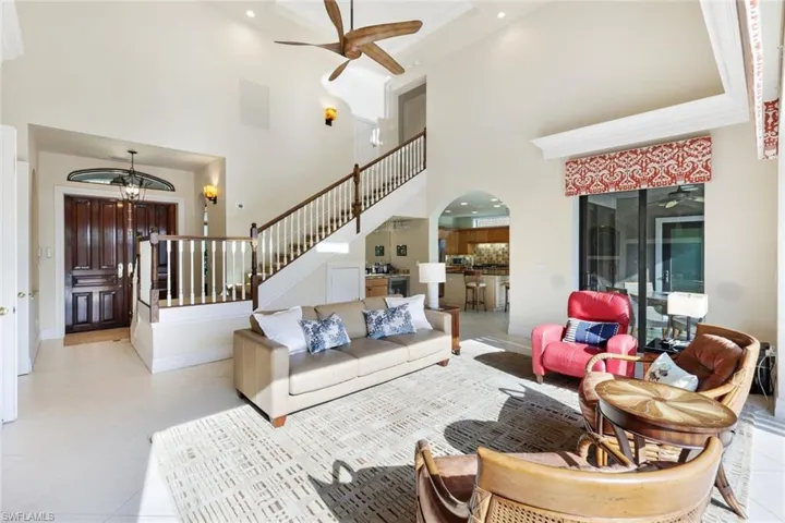 Tiled living room featuring a tray ceiling, ceiling fan with notable chandelier, and a high ceiling