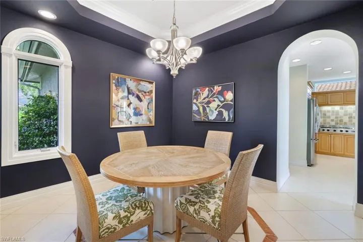Tiled dining space featuring a raised ceiling, a chandelier, and ornamental molding