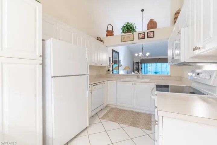 Kitchen with white cabinets, white appliances, sink, hanging light fixtures, and light tile patterned floors