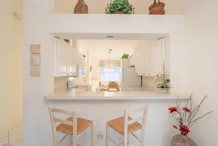 Kitchen with white appliances, a breakfast bar, kitchen peninsula, hanging light fixtures, and white cabinets