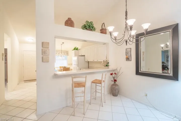 Kitchen with white refrigerator, vaulted ceiling, kitchen peninsula, light tile patterned floors, and white cabinetry