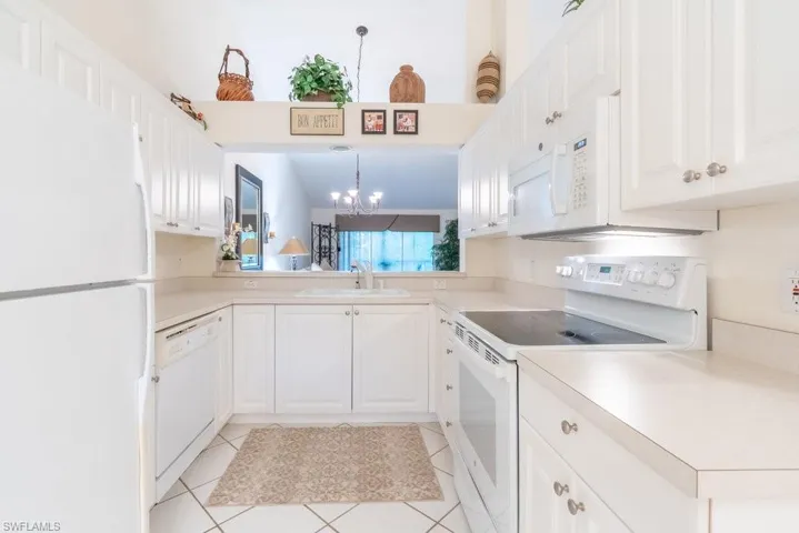 Kitchen with white appliances, white cabinetry, light tile patterned floors, and decorative light fixtures