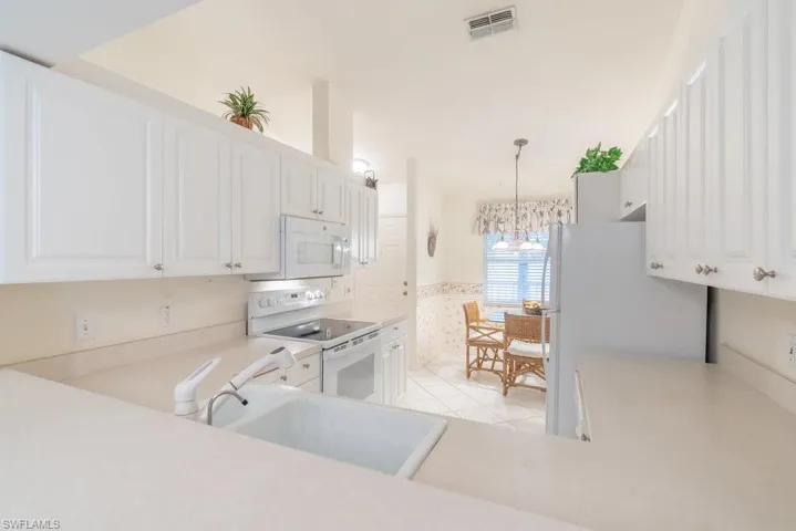 Kitchen with an inviting chandelier, white appliances, sink, hanging light fixtures, and white cabinets
