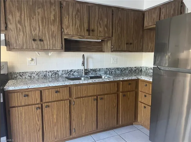 Kitchen featuring freestanding refrigerator, decorative backsplash, light stone counters, and light tile patterned floors
